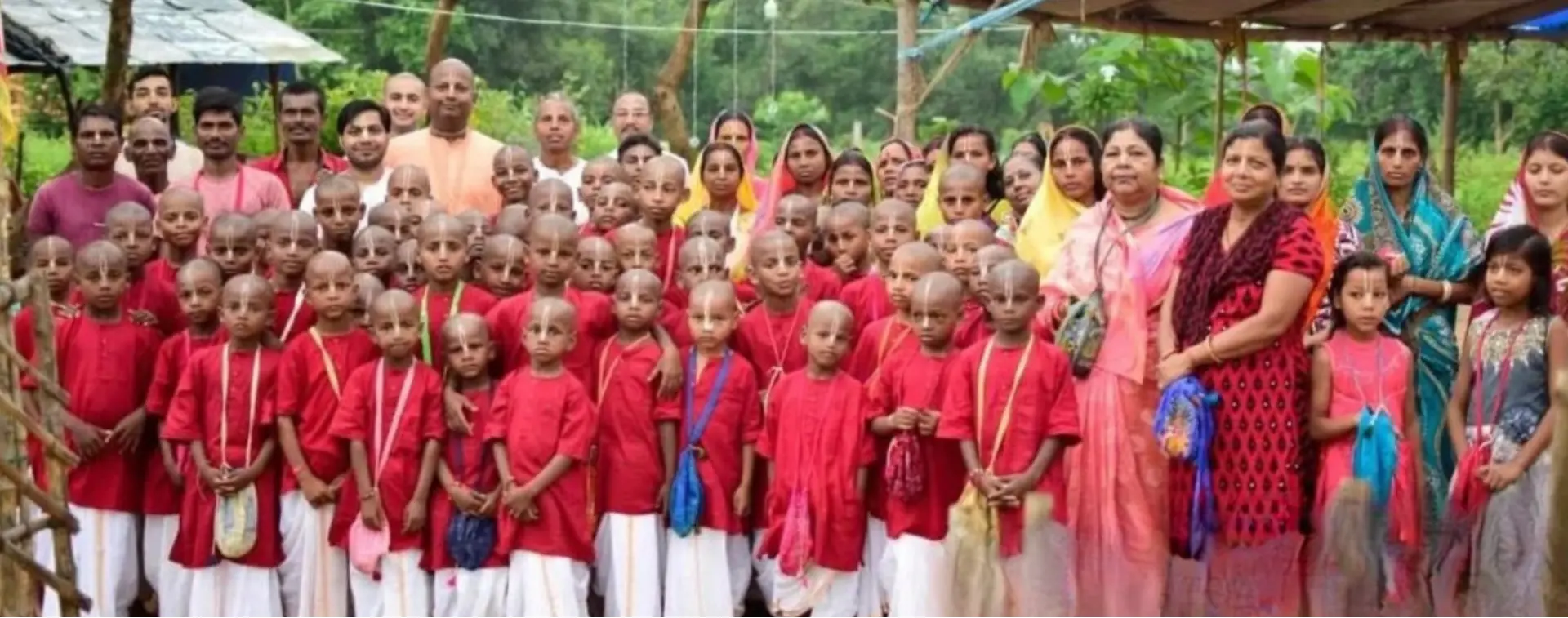 Large gathering of gurukul students and villagers under a thatched shelter